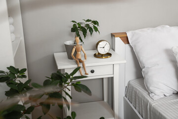 Bedside table with alarm clock, statuette and houseplant near white wall