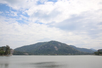 A peaceful lake reflecting the sky, surrounded by lush green mountains under a partially cloudy sky. The serene landscape exudes tranquility, making it a perfect nature escape and a picturesque travel