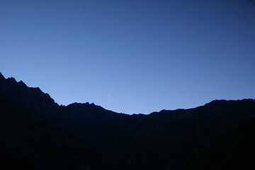 Obraz premium A serene twilight scene over a mountain ridge, with the last light of day fading into the deep blue sky. A single bright star appears in the evening sky, adding a touch of wonder to landscape.