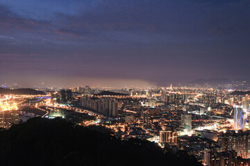 Night cityscape from mountain top. City lights glow in the valley under twilight sky, Shizaitou Mountain, Xindian, New Taipei City, Taiwan.