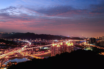 Fototapeta premium A stunning cityscape at dusk featuring brightly lit highways and high-rise buildings. Shizaitou Mountain, New Taipei City, Taiwan.
