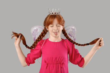 Cute redhead girl dressed as fairy with pigtails on grey background