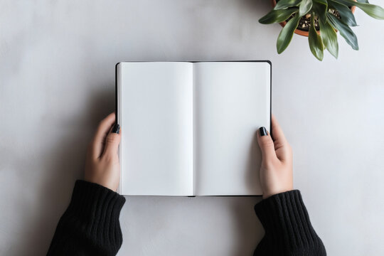 Hands holding an open blank book, top-down view.