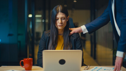 Businesswoman in a black blazer and yellow blouse sits at a desk with a laptop, looking...