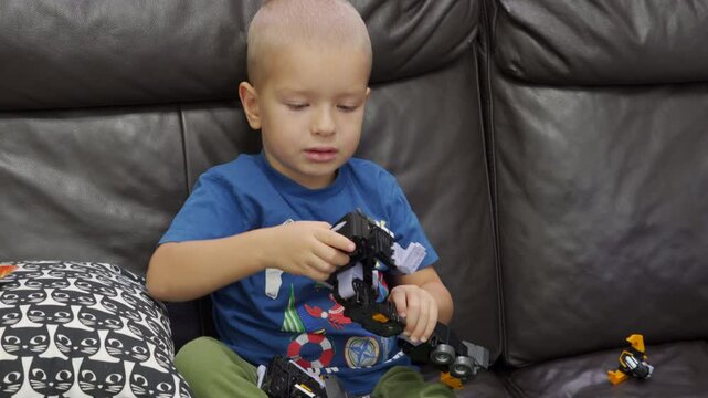 Child playing with new toy sitting on sofa at home. Concentrated face of little boy holding transformer robot toy. Three year old child examining new toy comments on his actions.