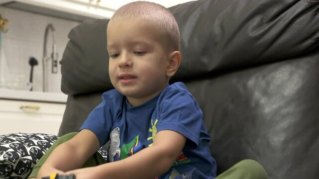 Child playing with new toy sitting on sofa at home. Concentrated face of little boy holding transformer robot toy. Three year old child examining new toy comments on his actions.