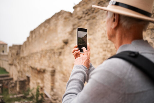 Tourist elderly man taking photo on smartphone, sightseeing taking picture with mobile phone in Akkerman fortress, Ukraine.