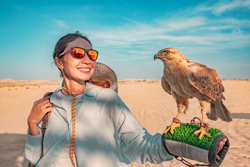 Smiling tourist holding a falcon on her arm while enjoying the sunny desert landscape of the United...