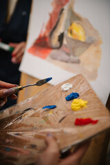 Girl mixing and combining colors. Woman painting in a workshop. Female is drawing a picture in art class. Art lesson. Education and learning concept. Hands drawing with brush on easel. Closeup.