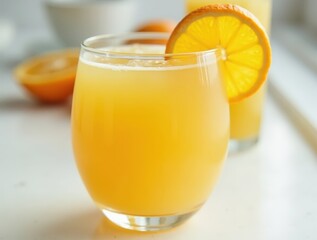 Fresh orange juice in glass with slice on rim on white table
