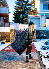 Chic woman strolls snowy street. A fashionable woman walks on a snowy path wearing a long black...