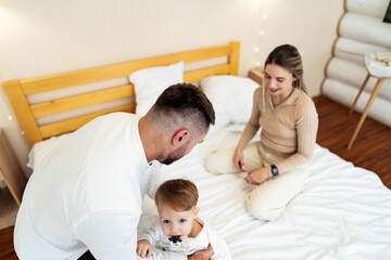 Obraz premium Cozy bedroom fun with toddler. Parents engage playfully with their toddler on a bed in a bright, cozy bedroom, creating joyful moments together.