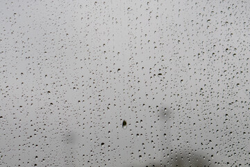 Raindrops on window glass against the moody grey British sky create a natural pattern. Water droplets on a transparent surface capture the minimalist texture during typical overcast weather