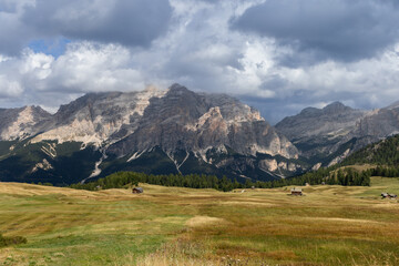 Obraz premium Autumn view of the Pralongia Plateau in the Dolomites, Italy. Features golden meadows, scattered alpine huts, and towering mountain peaks