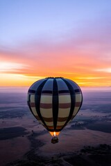 hot air balloon rises gently against backdrop of vibrant sunrise filling sky with vivid hues as it drifts peacefully