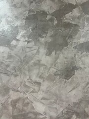 A textured gray surface with a mottled appearance, resembling concrete or plaster, showcasing subtle variations in color and pattern.