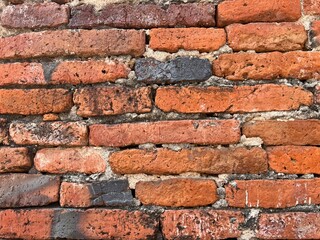 A close-up view of a textured brick wall featuring various shades of red and orange bricks, highlighting wear and age.