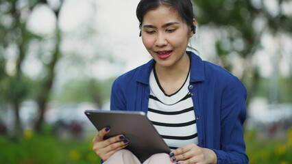 Fototapeta premium Asian woman effortlessly blending technology and nature, sitting on a bench with her laptop, showcasing the innovation of mobile work within an urban park setting.