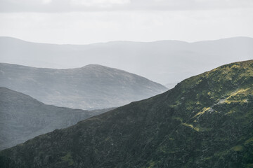 Lush green mountains with varying shades create a captivating view under a gentle cloudy sky. The landscape reveals a peaceful and tranquil environment, inviting exploration.