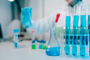Lab table with a blue beaker and a red dropper. The table is cluttered with various glassware and chemicals