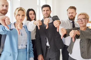 Group of professionals standing together in office, all showing thumbs down gesture. Young business...