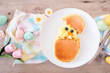 Fun Easter breakfast. Hatching scrambled egg chick and pancake egg. Above view table scene with a wooden background.