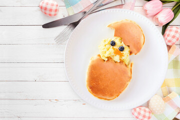 Fun Easter breakfast. Hatching scrambled egg chick and pancake egg. Overhead view table scene on a white wood background with copy space.