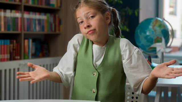 Sad upset Caucasian teenager junior school little girl child doubtful student kid schoolgirl pupil looking at camera dont know answer shrugging shoulders gesture fail exam mistake in library classroom