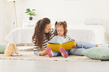 Happy smiling mother and baby daughter, babysitter nanny enjoy book story reading, friendly loving...