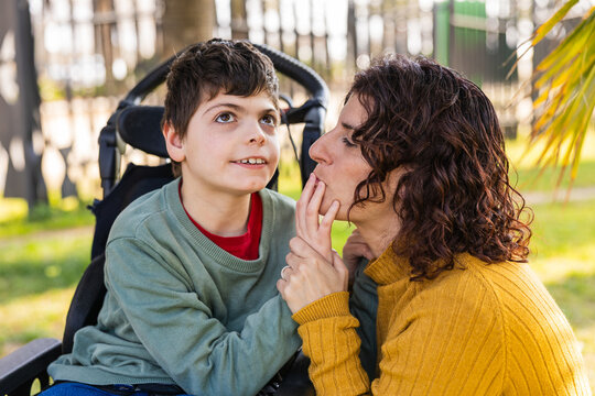 child with disability playing with mother in wheelchair at park