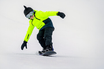 Young snowboarder in bright neon jacket riding downhill on snowy slope