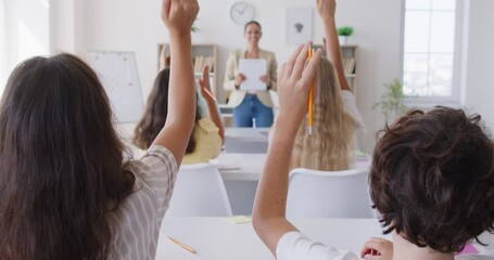 High school students sitting back at desks in classroom with woman teacher and raising hands up to ask or answer a question during a lesson. Back to school concept. 4k video. slow motion video.