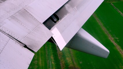 Airplane wing with flaps and spoilers extended during takeoff, flying over the green fields, offering a unique perspective of air travel