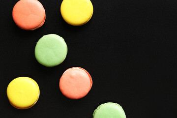Bright French macarons on a black background, top view. Assortment of multi-colored macarons with different flavors. Delicious pastries, flat lay. Food background. Sweets