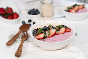 Presented by fruits putting yogurt toppings with strawberry, berry, oats, raisins and chia seed decorated by peppermint in white blow. Pink background. Set of healthy dairy product choice. Pecuniary.