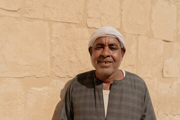 Photo of an Arab man wearing a white turban and traditional clothing with traditional patterns, smiling as he poses for the photo. Travel to Egypt. Valley of the Kings