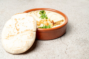 Delicious hummus with pita bread, chickpeas, and parsley in terracotta bowl