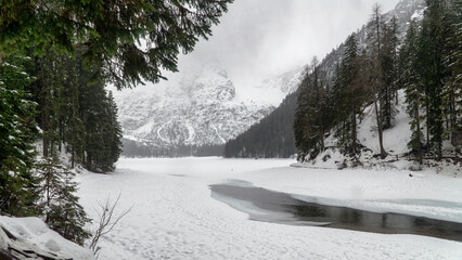 Frozen lake surface covered with snow. Foggy, rainy, winter landscape. Lake Braies, Lago di Braies in winter, Dolomites, Italy, Europe.