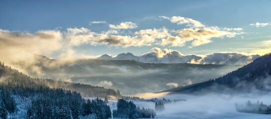 Mountain valley shrouded in mist at sunset in winter. Thick mist envelops the valley at dusk, mountains picks on horizon,  clouds on blue sky. South Tyrol, Trentino Alto Adige, Alps, Italy, Europe.