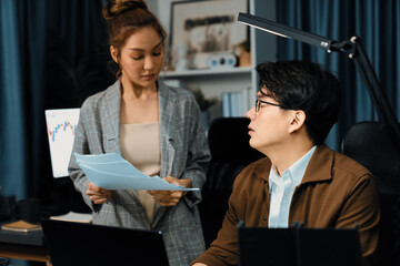 Managers discussing on document paperwork together for business planning on market share data at over late night time at modern home office, working on startup company deadline project job. Infobahn.