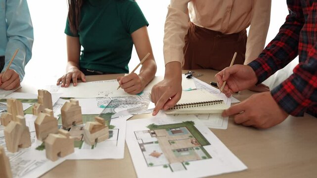 Smart architect and safety engineer discussion about building blueprint on table with architectural document, measurement tools and wooden block scatter around at modern office. Closeup. Delineation.