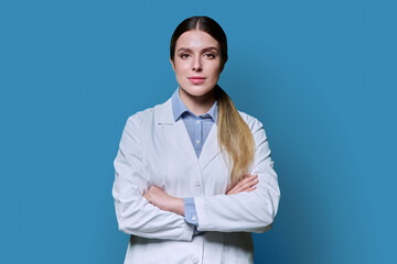 Portrait of young female student intern in white lab coat on blue background