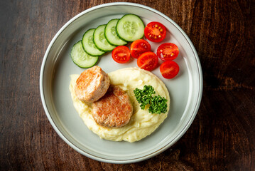 A delicious plate of meatballs served with creamy mashed potatoes and a fresh side of cucumber slices and cherry tomatoes, garnished with parsley.