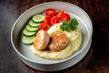 A delicious plate of meatballs served with creamy mashed potatoes and a fresh side of cucumber slices and cherry tomatoes, garnished with parsley.