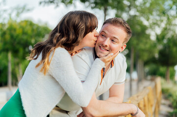Fototapeta premium Romantic Couple Kissing in a Park: Woman Kissing Man's Cheek