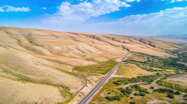 Aerial view of arid mountainous landscape with winding road under blue sky