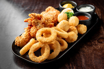A delicious platter of crispy fried chicken wings, onion rings, and golden mash balls, accompanied by dipping sauces and garnishes, perfect for sharing or a hearty meal.