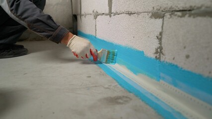 Construction worker applying waterproofing paint on basement wall