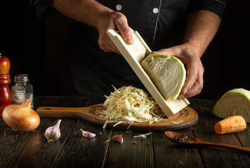 A mountain of shredded cabbage on a kitchen board. A chef prepares raw cabbage for cooking. Shredding cabbage with a hand grater.