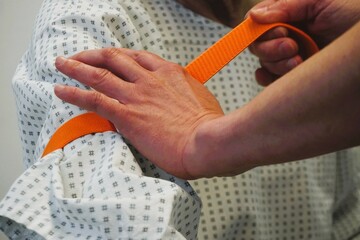 Ärztin drückt Oberarm von Patientin mit Band ab für Infusionsgabe im Krankenhaus 
